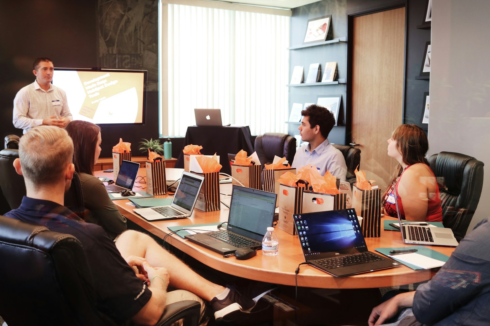 A team meeting around a table, one colleague presenting from a laptop